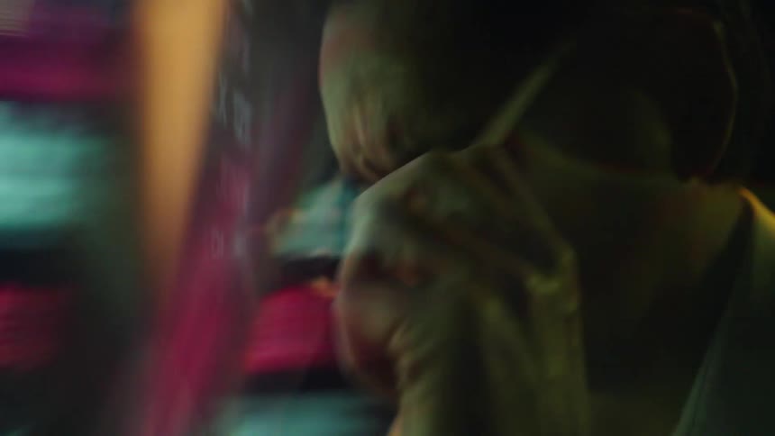 A man wearing glasses and a light shirt looks tired in front of a screen displaying red and green financial data in a dark room with colorful reflections on his face