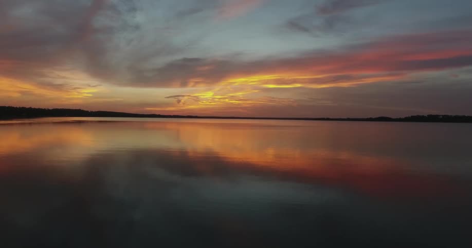 The sunset colors and clouds are reflected on the water's surface