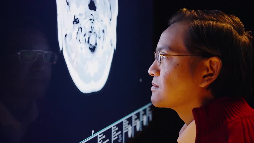 Man wearing glasses and red sweater observes a brain mri scan on a monitor