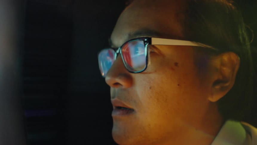 A man wearing glasses looks intently at a digital screen displaying stock charts and data