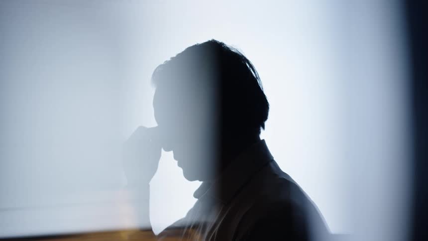 Silhouette of man with hand on forehead against a bright background