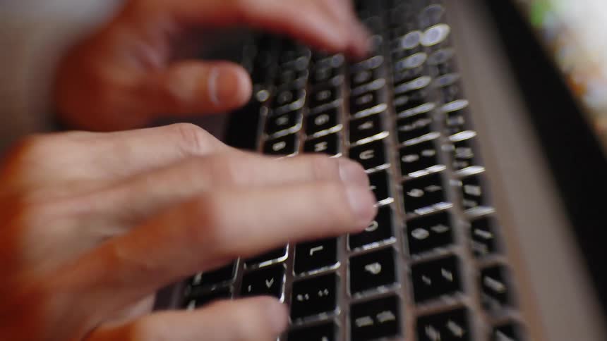 Blurred hands type on a keyboard under warm lighting