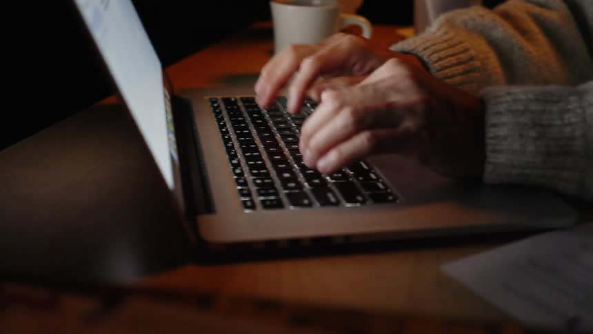 Hands typing on a laptop on a desk with a cup in the background