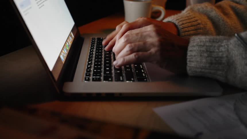 Person typing on a laptop on a desk with documents beside it