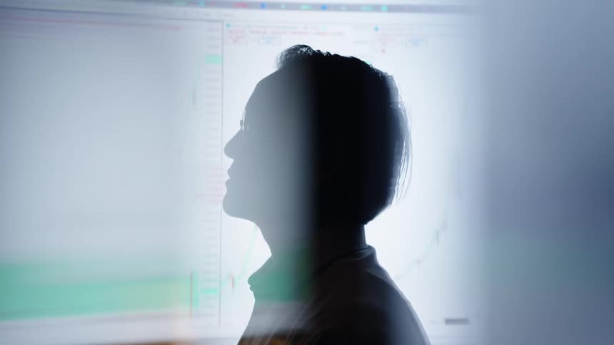 Silhouette of a person in front of a monitor displaying financial charts on the screen