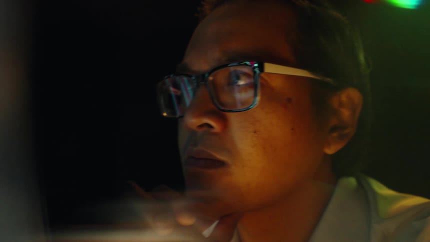 Man wearing glasses analyzes financial charts on an illuminated screen