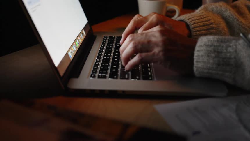 Hands type on a laptop on a desk with a cup in the background
