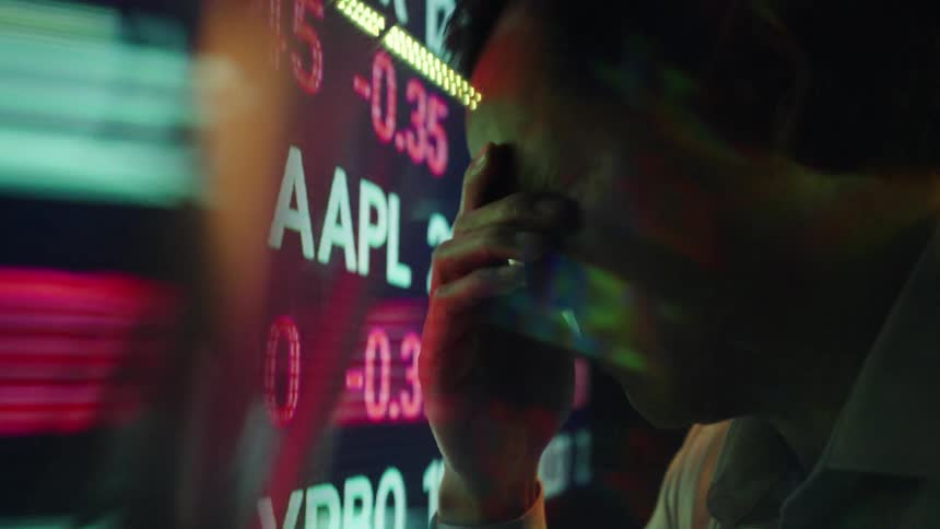 Digital numbers and letters move across a large screen as a man takes off his glasses and rubs his eyes