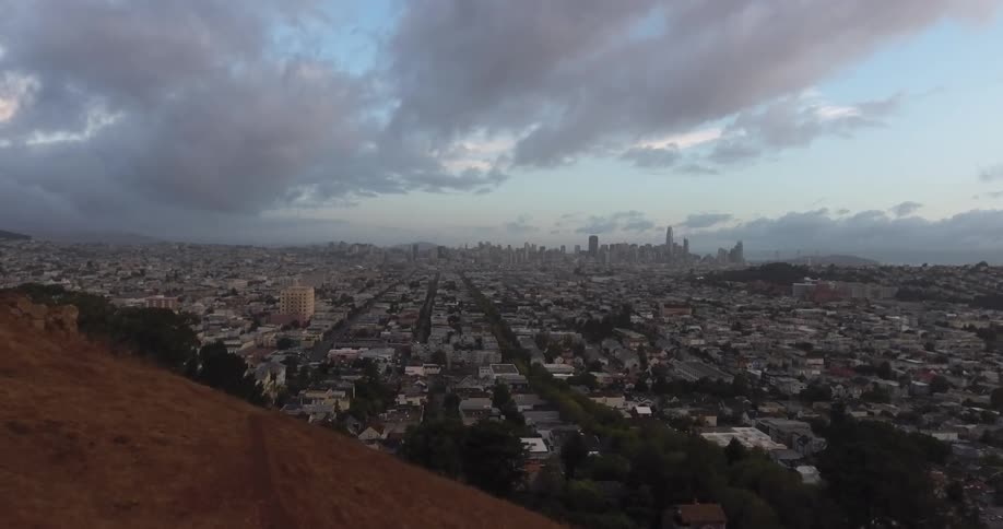 Clouds hover over a city in the distance that spans out from the hills into a valley