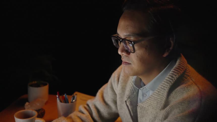 Man wearing glasses working at a desk under focused lighting