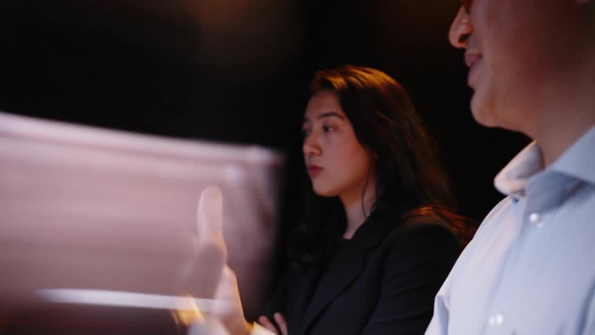 Two business people interact with a large digital screen displaying financial charts and graphs in a dark room