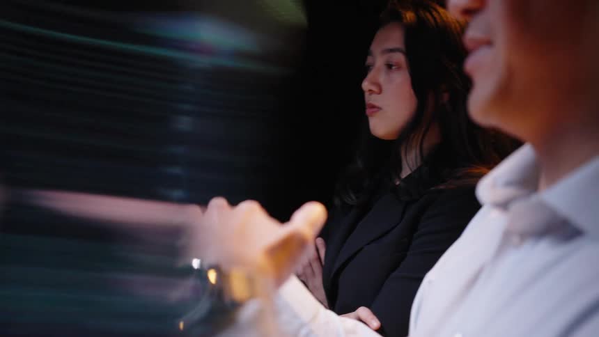 A close view of a man and a woman in a dark room shows the man talking and gesturing while the woman looks on from the background as motion blur and light leak effects move across the frame