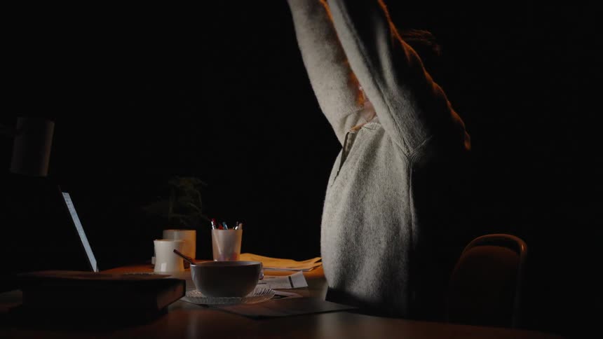 Man sitting at a desk covers his mouth while yawning in front of a laptop