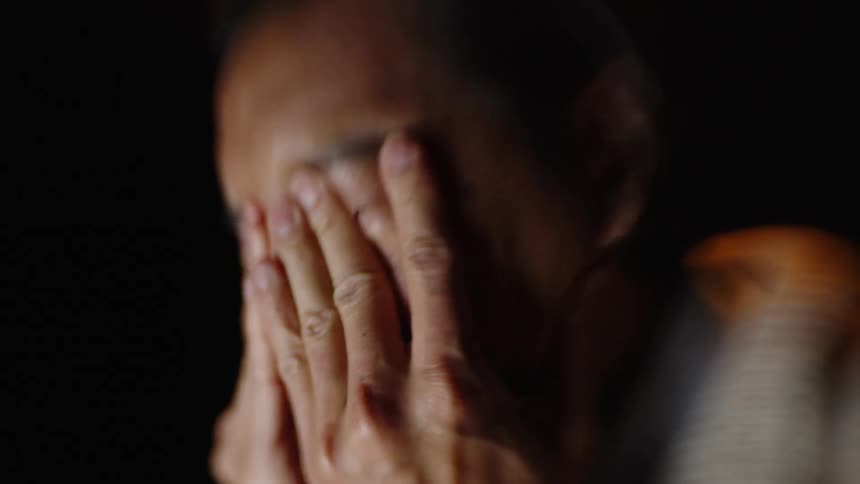 Man covers his face with his hands in a dark environment