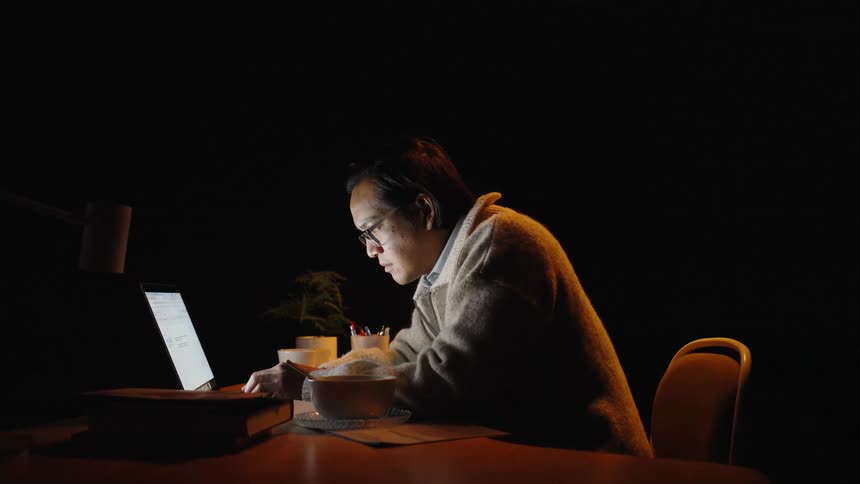 Man leaning over an illuminated laptop at a desk at night