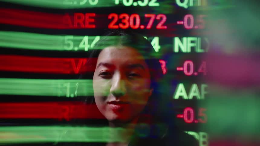 A woman with long dark hair is seen while glowing stock market tickers and financial data move across the screen