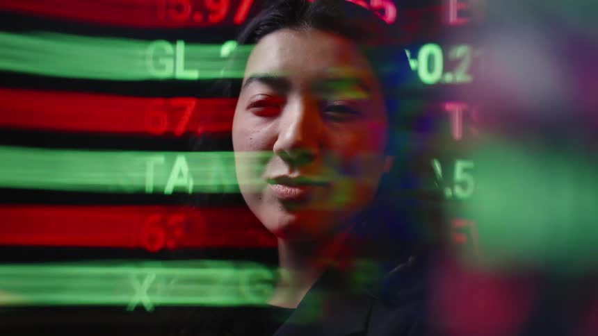 A woman with long dark hair is seen while glowing stock market tickers and financial data move across the screen