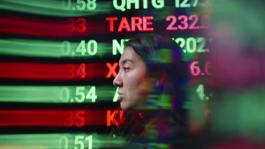 A woman with long dark hair is seen while glowing stock market tickers and financial data move across the screen