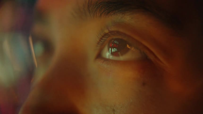 The video features a tight closeup of a persons eye focusing on the reflection on the cornea within this reflection scrolling lines of text and data are visible suggesting the person is looking at a digital screen or interface