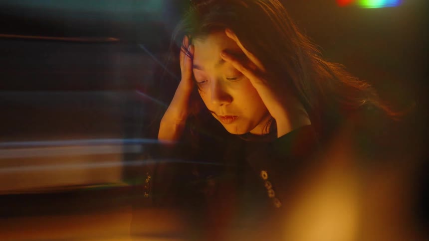 Woman presses her temples in front of projected financial charts