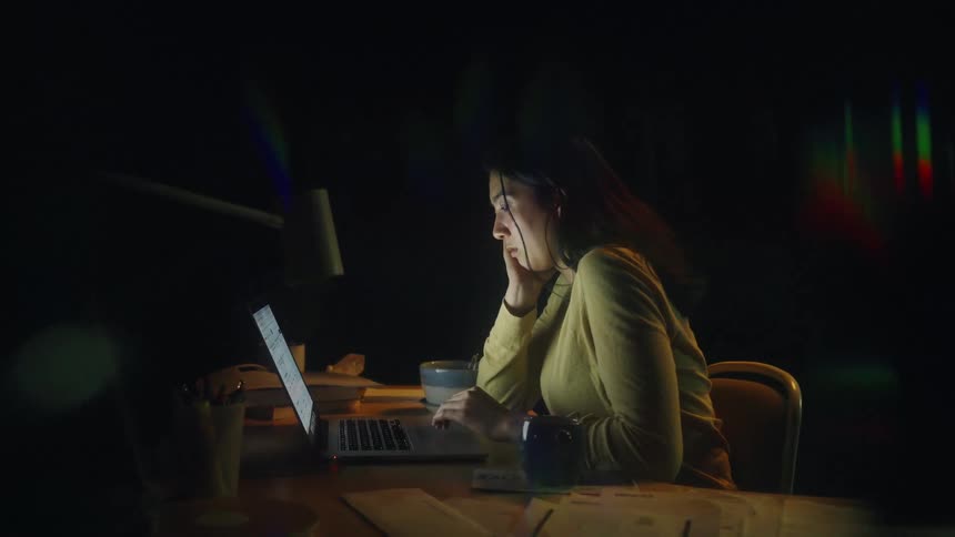Woman works on a laptop at night with documents spread across the desk