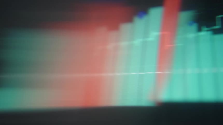 A rapid closeup pan sweeps across a digital trading screen showcasing glowing teal and red bar graphs alongside fluctuating data lines that are softened by heavy motion blur and vibrant light streaks as the interface updates
