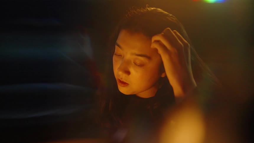 Woman touches her forehead under warm lighting in a dark environment