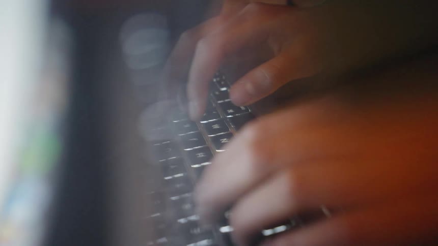 This video shows a closeup slightly blurred shot of someone typing quickly on a backlit laptop keyboard the visual style uses a doubleexposure or motionblur effect creating a sense of rapid movement and focused activity in a dark environment