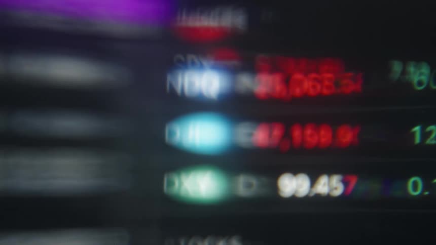 A close view shows blurry digital graphs and stock market data with red and green bars moving quickly across a dark screen