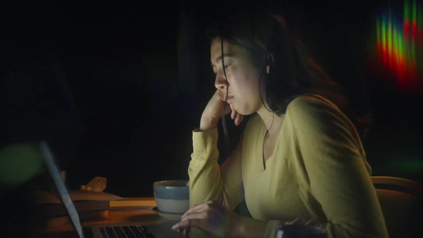 Woman sitting at a desk works on a laptop under nighttime lighting