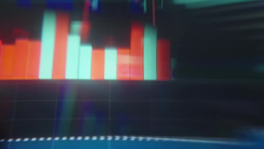 A close view shows blurry digital graphs and stock market data with red and green bars moving quickly across a dark screen