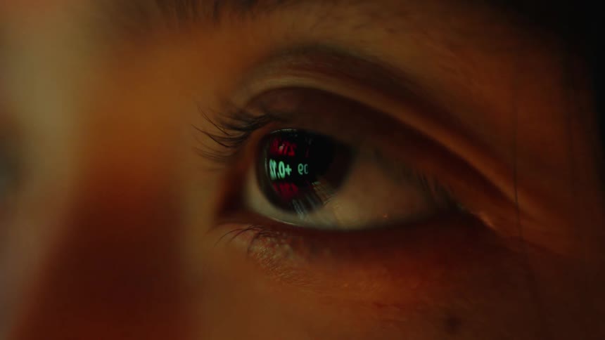 A persons face with eyes open as they blink staring at a screen that reflects on their face