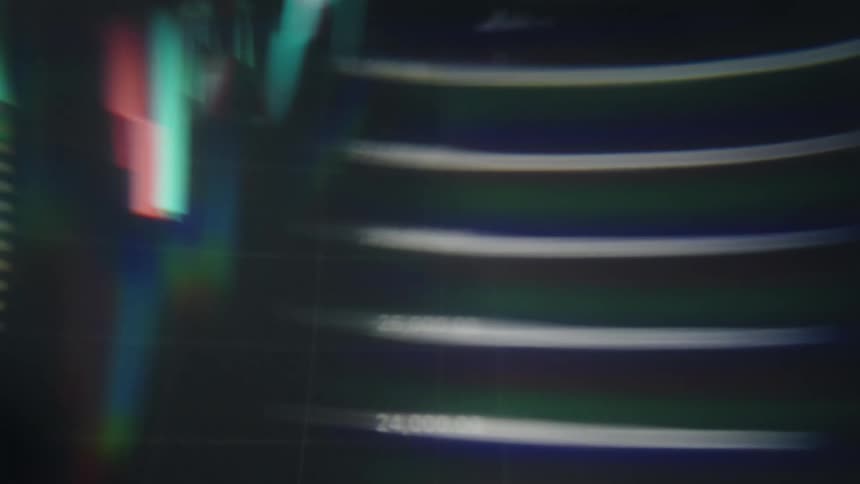 A close view shows blurry digital graphs and stock market data with red and green bars moving quickly across a dark screen