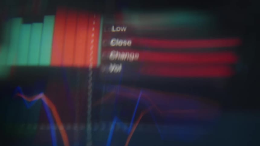 A close view of a glowing computer screen displays colorful digital stock market charts and data with motion blur and light leak effects across the frame