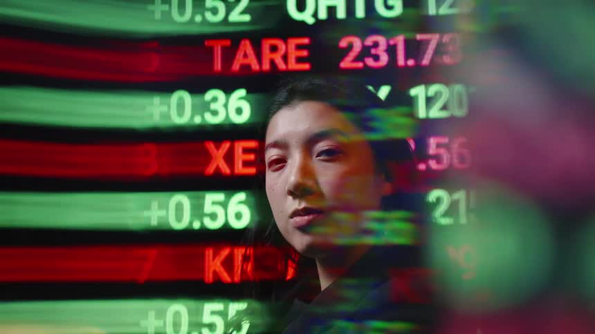 This video features a woman looking thoughtfully at a digital stock market ticker display as it scrolls across the screen the vibrant colorful data points reflecting off her face emphasize the fastpaced and immersive nature of the financial world
