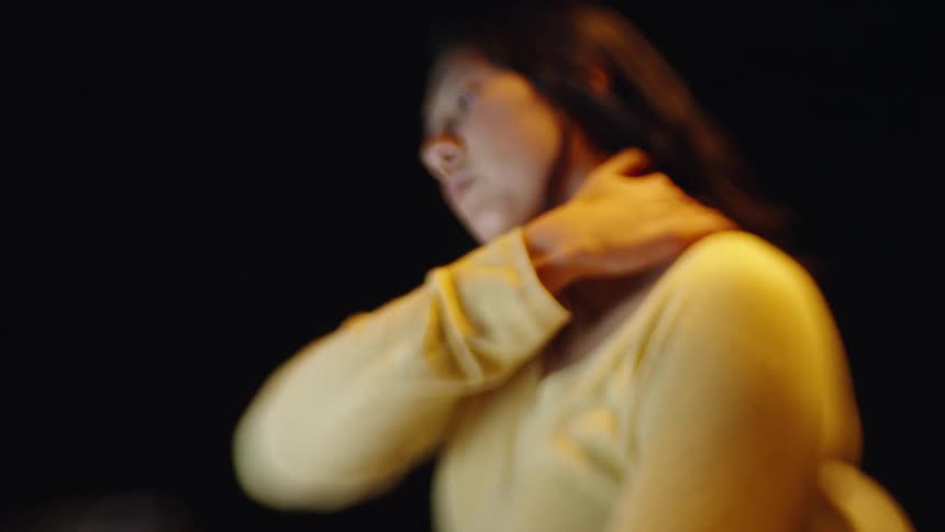 A softly blurred image shows a woman in warm lighting lifting her hand to her head against a dark background