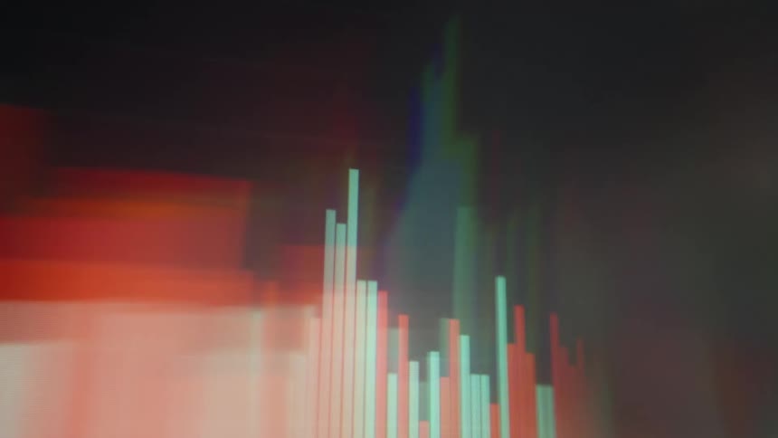 A close view shows blurry digital graphs and stock market data with red and green bars moving quickly across a dark screen