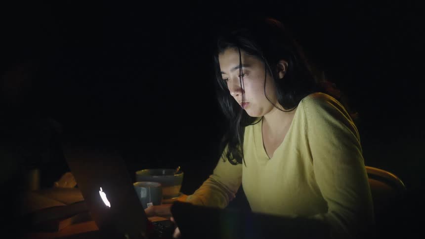 The woman leans over her laptop while typing