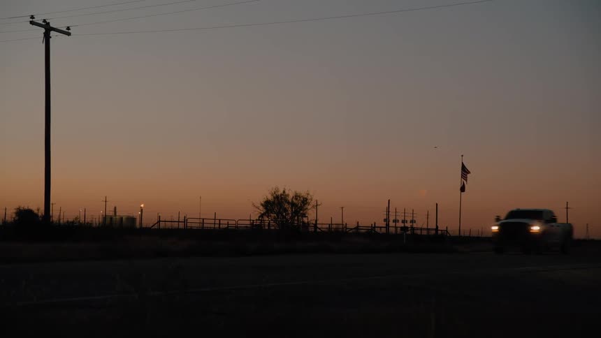 Truck travels on a rural road with a fence and utility poles as flags move in the wind