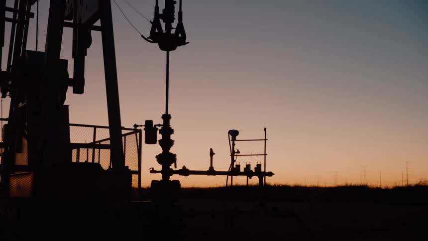 A silhouette of an oil pump jack operates against a gradient sunset sky