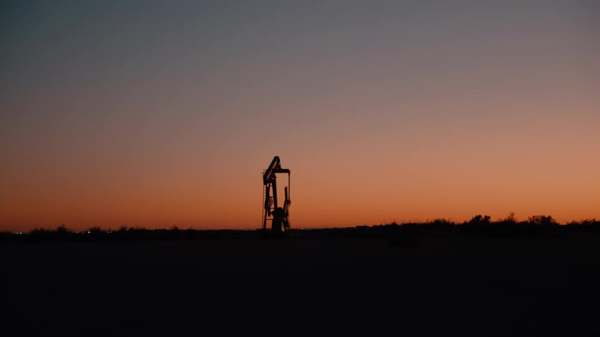 The sun is rising on the drilling rig in the distance