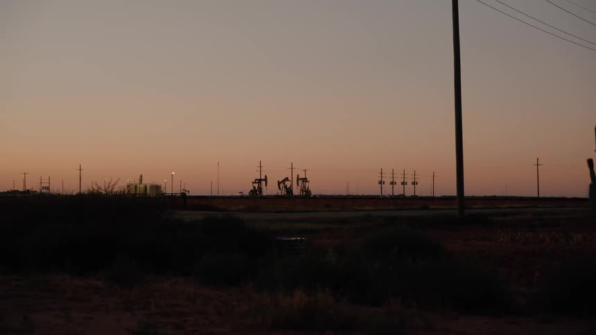 Oilfield equipment working on the side of a rural road near utility poles
