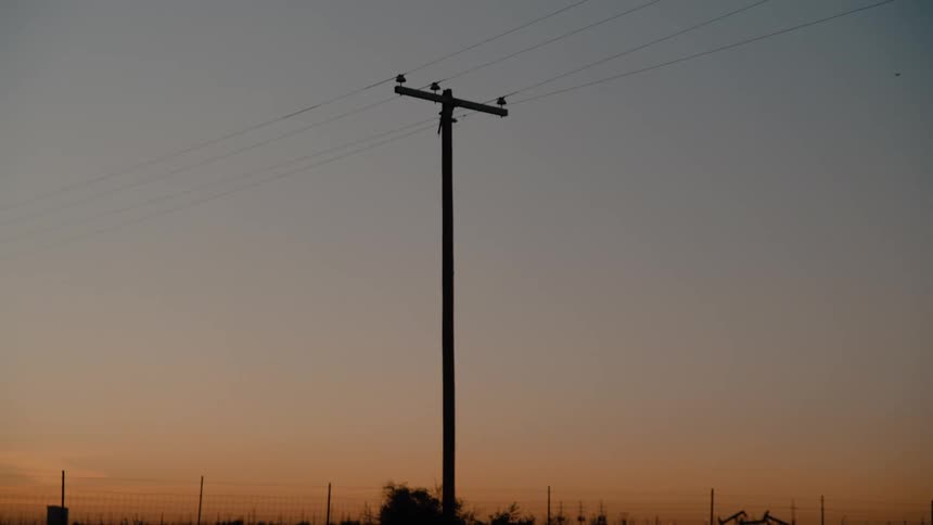 A silhouette of a utility pole stands against a gradient sky at dusk