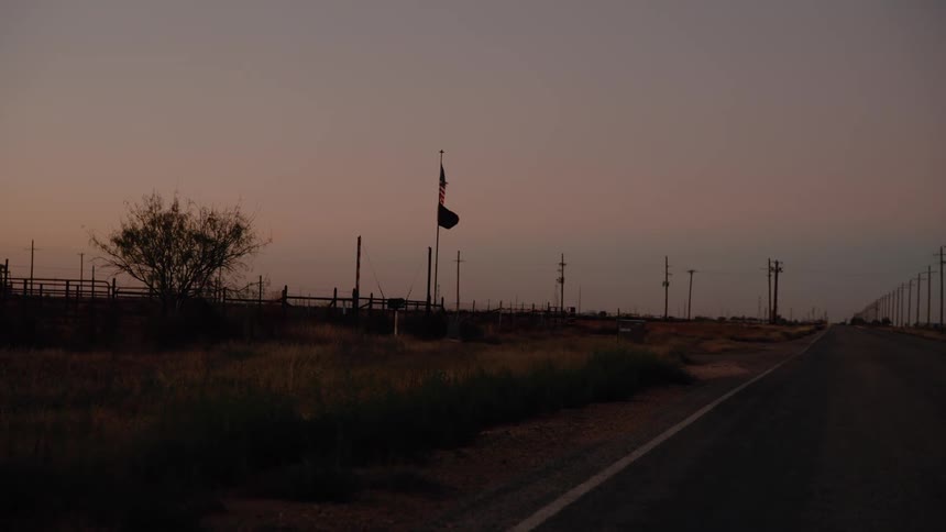 Fence and utility poles on top of a hill as flags move in the wind