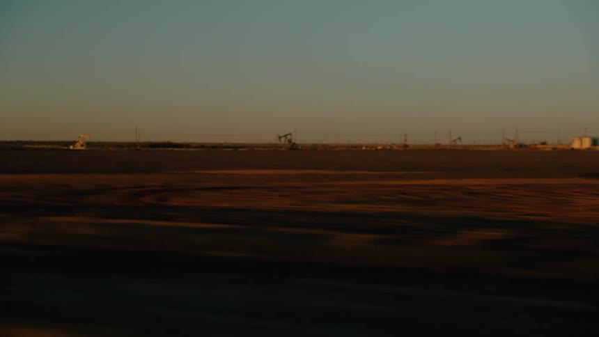 Oilfield equipment working on the side of a rural road near utility poles