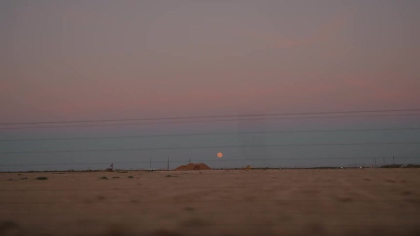 Arid landscape at dusk with a low moon on the horizon