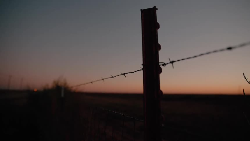 Fence post with barbed wire silhouetted against the sky at dusk