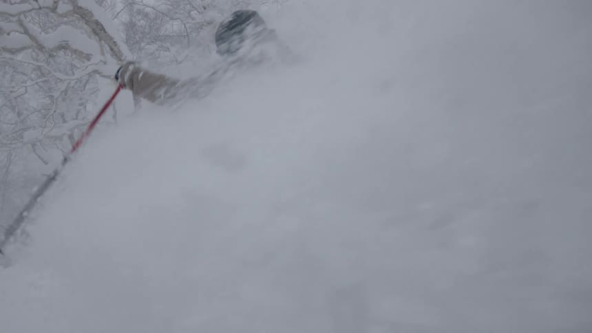 Snow flies as a skier holds their poles sliding down a mountainside during a blizzard