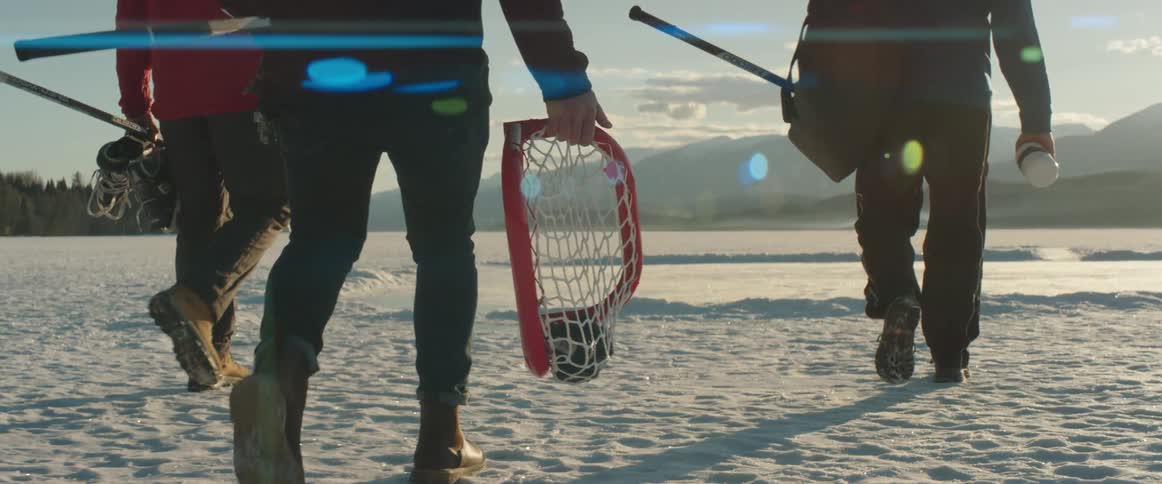 People walk on a frozen lake carrying a hockey net and equipment