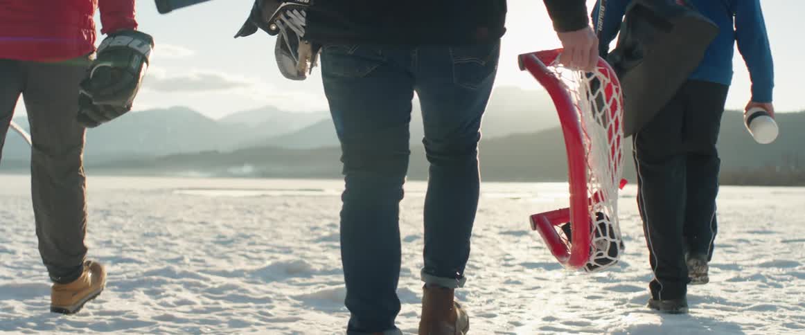 People walk on a frozen lake carrying a hockey net and sticks